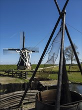 A traditional windmill stands proudly next to fishing nets against a green landscape and blue sky,