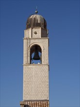Close-up of a bell tower with visible bell and clear blue sky, the old town of Dubrovnik with