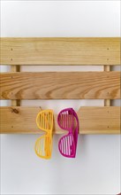 Funny colorful plastic glasses hanging on a wooden shelf on a white wall