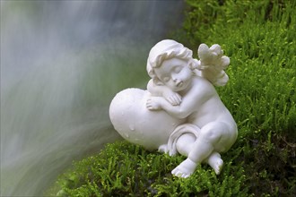 Porcelain angel figurine on moss by a waterfall