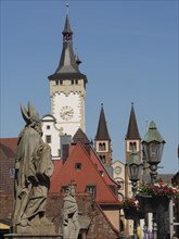 Historical statues in front of a clock tower, church towers and lanterns with flowers, blue sky in