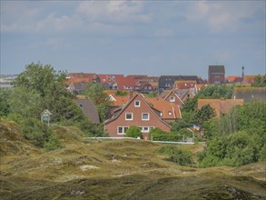 A village with red roofs, nestled between green hills and trees, Baltrum Germany