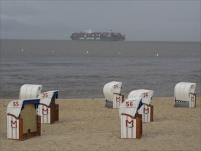 Several beach chairs on the beach under a cloudy sky with a large ship on the sea in the distance.