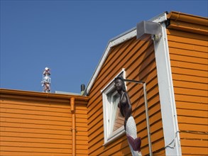 An orange-coloured house wall with a statue of a mermaid in front of a clear blue sky, Heligoland,
