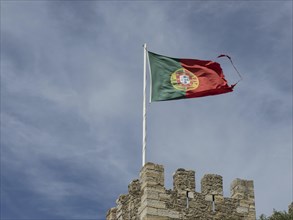 Portuguese flag flying on a medieval castle tower under a slightly cloudy sky, Lisbon, Portugal,