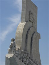 A large stone monument with many detailed human figures and a leading figure, the sky is clear and