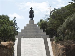 Large historical monument with a statue on steps, surrounded by nature and a clear sky, Corsica,