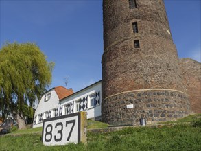 An old stone tower next to a house with the number 837 and a large, green pasture, rhine promenade