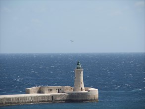 A lighthouse stands on a pier and looks out over the vast blue ocean, Valetta, Malta, Europe