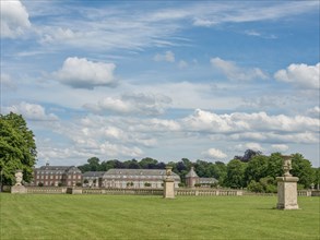 Sweeping view of a historic building, corridor of sculptures and green lawn, under an open sky with