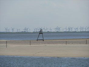 Sandy beach beach and the sea, in the background wind turbines under a slightly cloudy sky, Baltrum