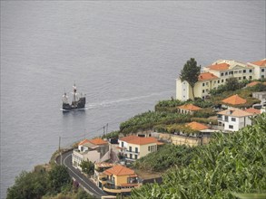 Coastal landscape with a town on a hill, many houses and a passing ship, Madeira, Portugal, Europe