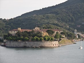 Fortress on the water with a sailing boat in the foreground, surrounded by trees and hills, Bari,