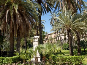 A tropical garden with tall palm trees and an ancient sculpture, palermo in sicily with an