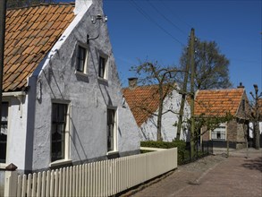 Two white houses with orange-coloured roof tiles along a quiet, sunlit street, Enkhuizen,