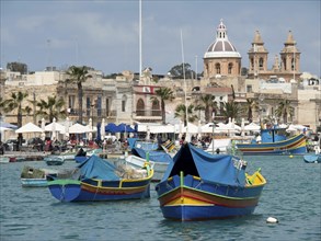 Colourful fishing boats and historic buildings with steeples on a sunny harbour, Valetta, Malta,