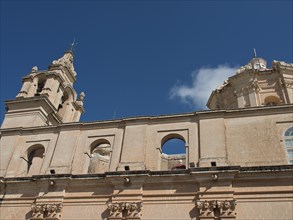 Baroque church with sandstone bell tower under a clear sky, the town of mdina on the island of
