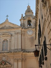 Partial view of a church with clock tower and bell tower against the blue sky, the town of mdina on