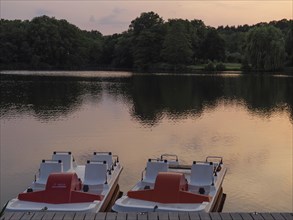 Pedal boats on the quiet lake at sunset, surrounded by nature, peaceful atmosphere, jetty on a