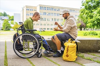 Man helping to eat to a man with cerebral palsy in a wheelchair in the university campus