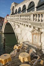 Rialto Bridge and Restaurant Tables on Grand Canal in a Sunny Day in Venice, Veneto, Italy, Europe