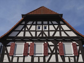 Half-timbered house with red shutters and tiled roof, under a clear blue sky, historic