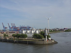 Harbour view with wind power plant, spherical tanks, containers and green trees under a clear sky,