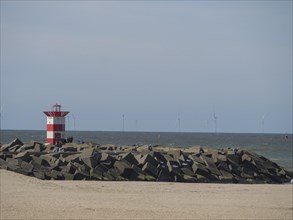 Lighthouse on the coast with breakwaters in the foreground and wind turbines in the background,