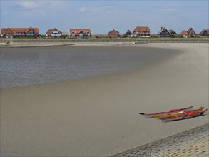 Quiet beach with kayaks on the shore, in the background houses and dunes under a blue sky, Baltrum