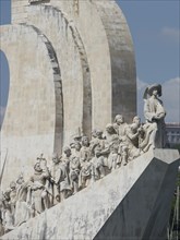 Large stone monument with numerous historical figures, including a man with a hat, in front of a