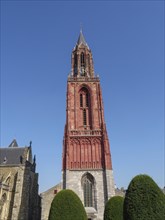 Red gothic church tower flanked by bushes under a clear blue sky, Maastricht, Netherlands