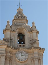 Bell tower of a baroque church with clock under a clear sky, the town of mdina on the island of