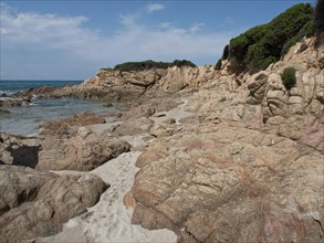A rocky beach with sandy areas, surrounded by dense vegetation and clear blue sea, Corsica,