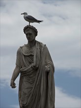 Antique statue with a seagull on its head in front of a cloudy sky, Corsica, Ajaccio, France,