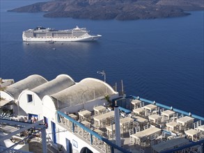 A cruise ship sails on the calm sea along a terrace of a restaurant on an island, The volcanic