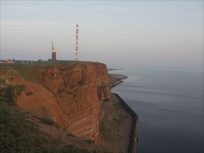 Red rock cliffs on the coast with a lighthouse and an antenna in the background at dusk looking out