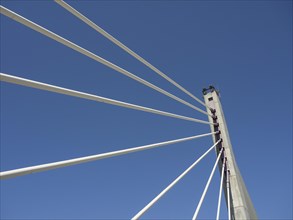 A modern bridge with interesting architecture and numerous cables in front of a clear blue sky,