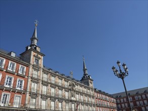 Historic buildings with red facades and towers under a bright blue sky in the Plaza Mayor, Madrid,