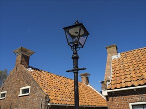 Historic street lantern in front of traditional brick houses with orange-coloured roof tiles,