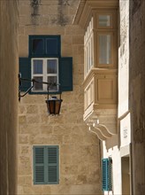 Narrow alley with old stone buildings, blue shutters and lanterns under the sun, the town of mdina