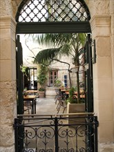 An inviting inner courtyard with palm trees is accessible through an iron gate, the town of mdina