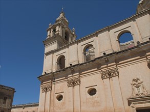Partial view of a historic church with a tower and a bright blue sky, the town of mdina on the