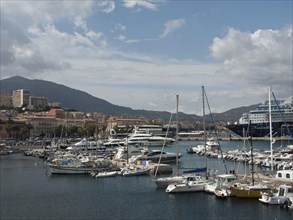 Harbour view with numerous boats and yachts in front of a mountain landscape and under a cloudy