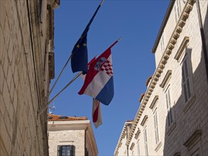 Flags of the European Union and Croatia fly in a narrow alley between historic buildings, the old