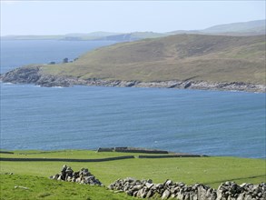 Coastal landscape with blue sea, green fields and hills in the background, green fields on the
