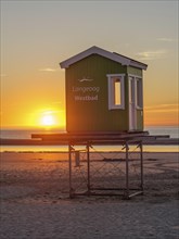 Beach hut at sunset, warm light bathes the scene in a cosy orange, setting sun on the North Sea