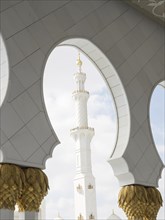 An impressive minaret of a mosque in bright white with golden details and a clear sky, Abu Dhabi,