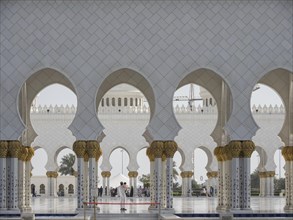 People pass elegant white arches with golden decorated columns in a magnificent architecture, Abu
