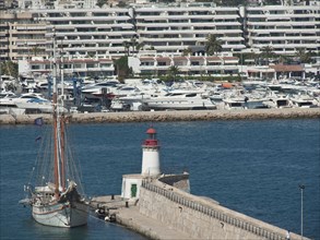 Harbour with a large sailing ship and a lighthouse, surrounded by blue buildings and yachts, ibiza,