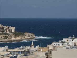 Town view of the open sea and waves crashing on the shore, the island of Gozo with historic houses,